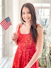 Load image into Gallery viewer, Top of red floral tiered tie mini dress with American flag in hand

