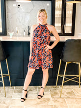Load image into Gallery viewer, front view of red and blue floral halter dress  standing in front of bar
