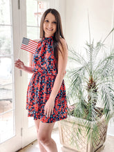 Load image into Gallery viewer, Standing in front of palm trees, red and blue floral halter mini dress with American flag
