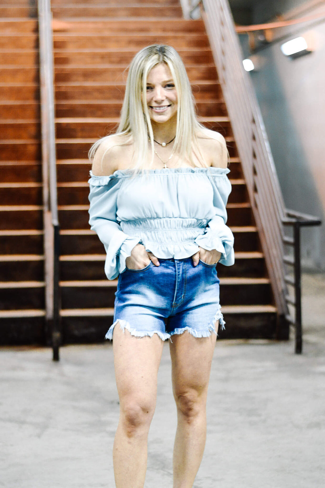 Women's ripped denim high waisted jean shorts. Paired with a smocked long sleeve blue off the shoulder women's blouse