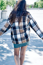 Load image into Gallery viewer, Back of women&#39;s brown, white and black plaid long sleeve button down shacket. Paired with a teal tshirt dress and white converse. 
